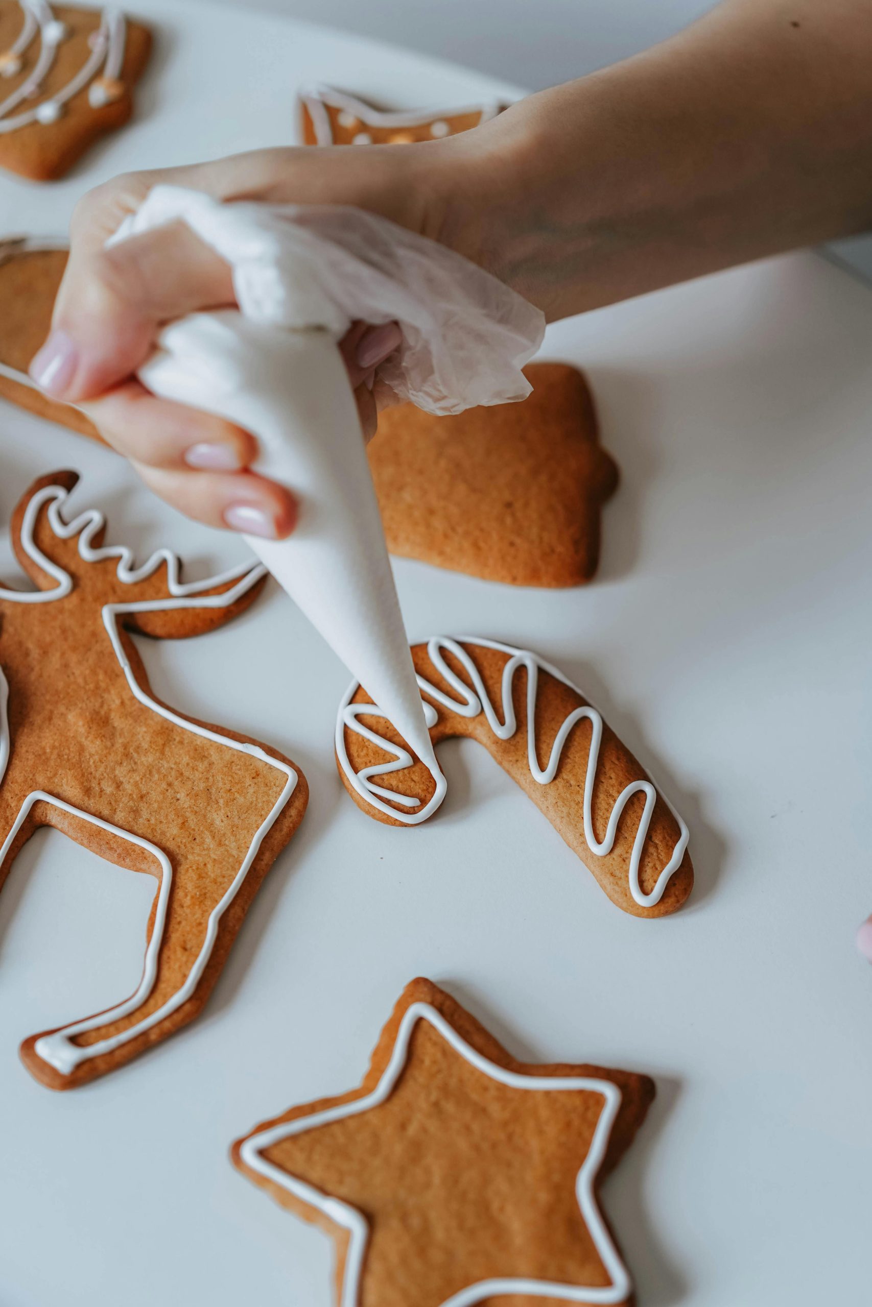 Close-up of a hand decorating gingerbread cookies with white frosting for Christmas.